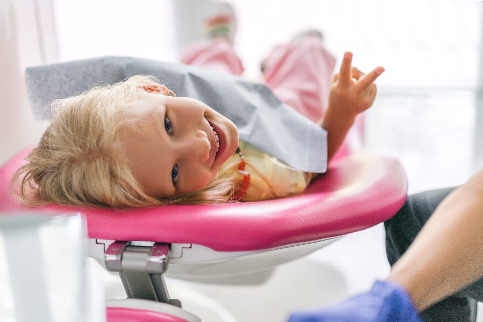 little girl lying in dental chair holding up a peace sign