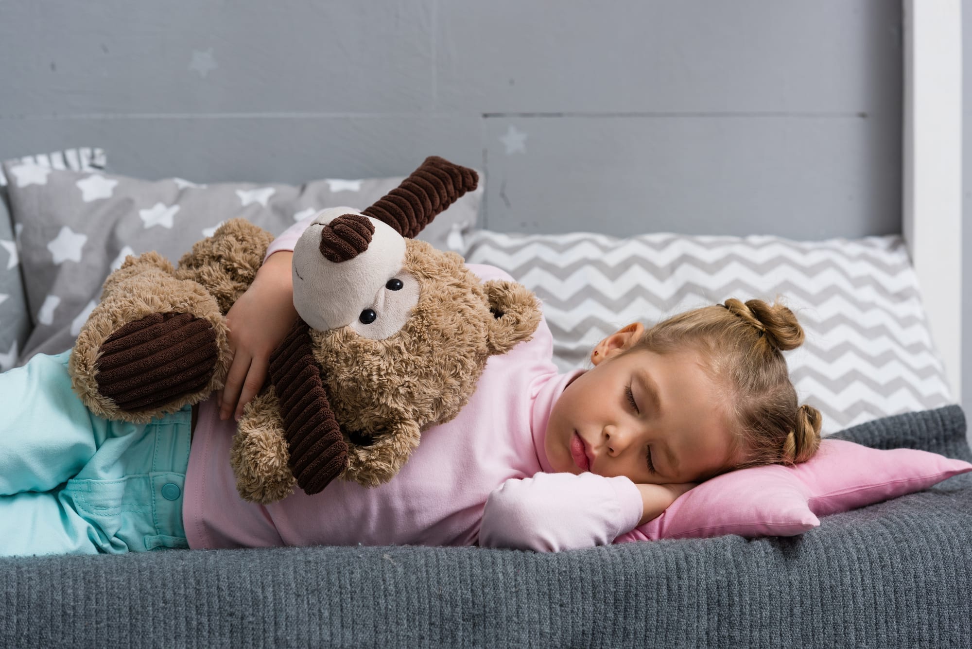 little girl sleeping with teddy bear on bed