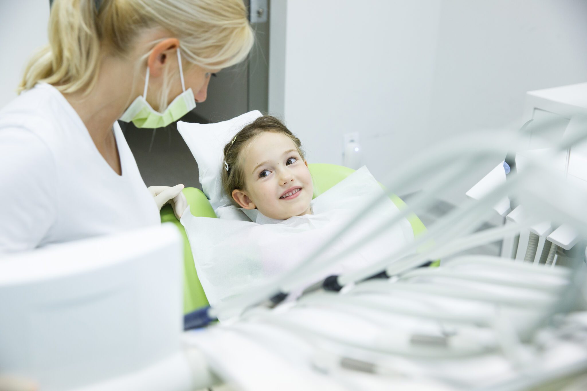 Little patient conversing with her dentist at dental office before her regular checkup for cavities and gum disease.