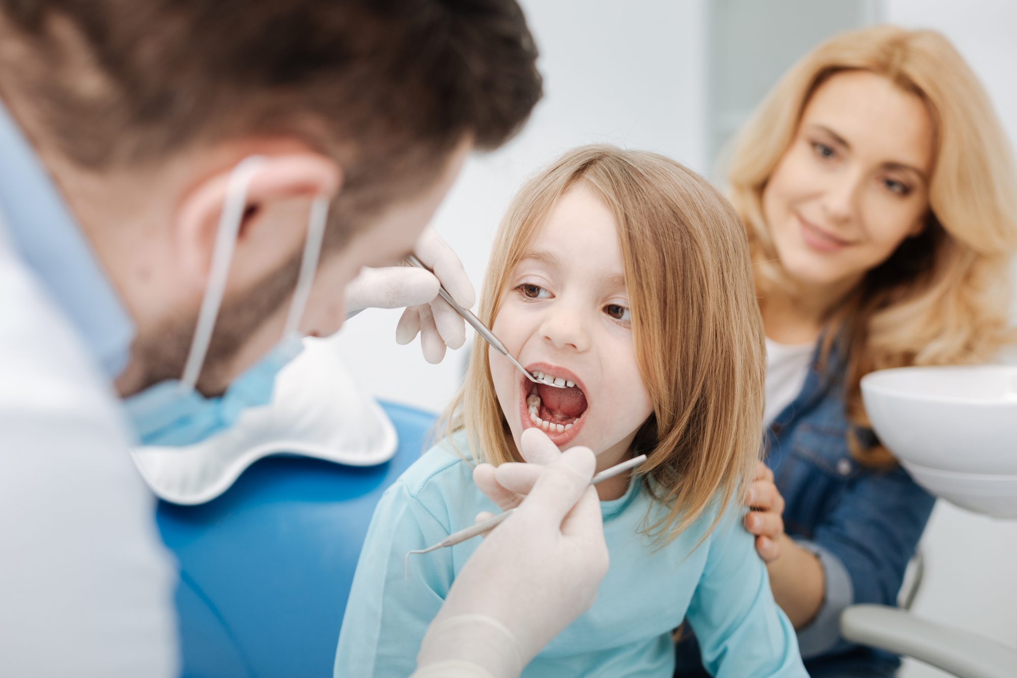 Young male pediatric dentist examining a little girl's mouth