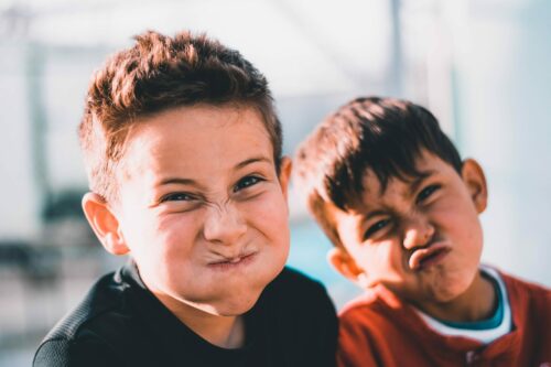 two young boys making silly faces and hiding their smiles