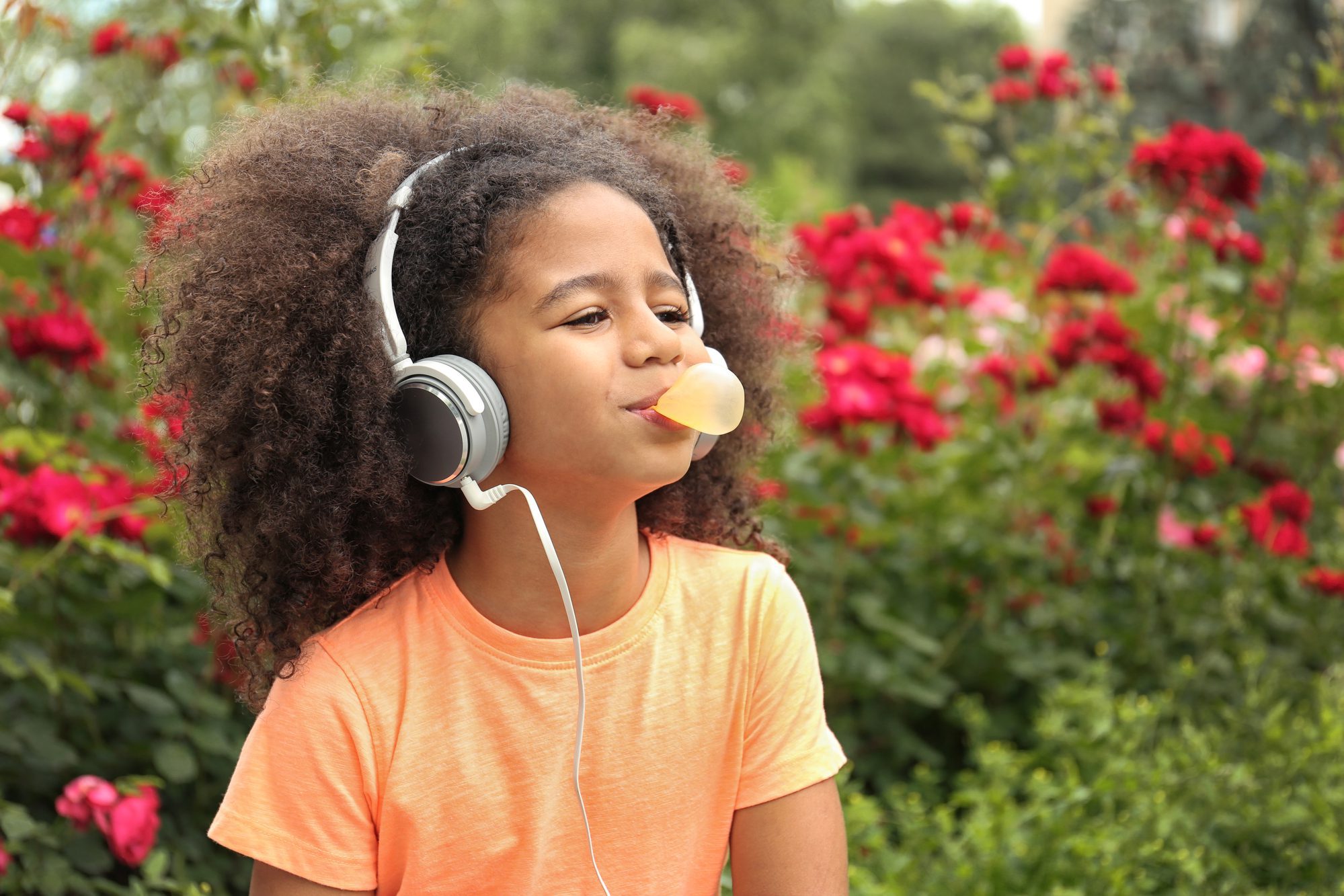 Little girl with headphones chewing bubblegum in the park