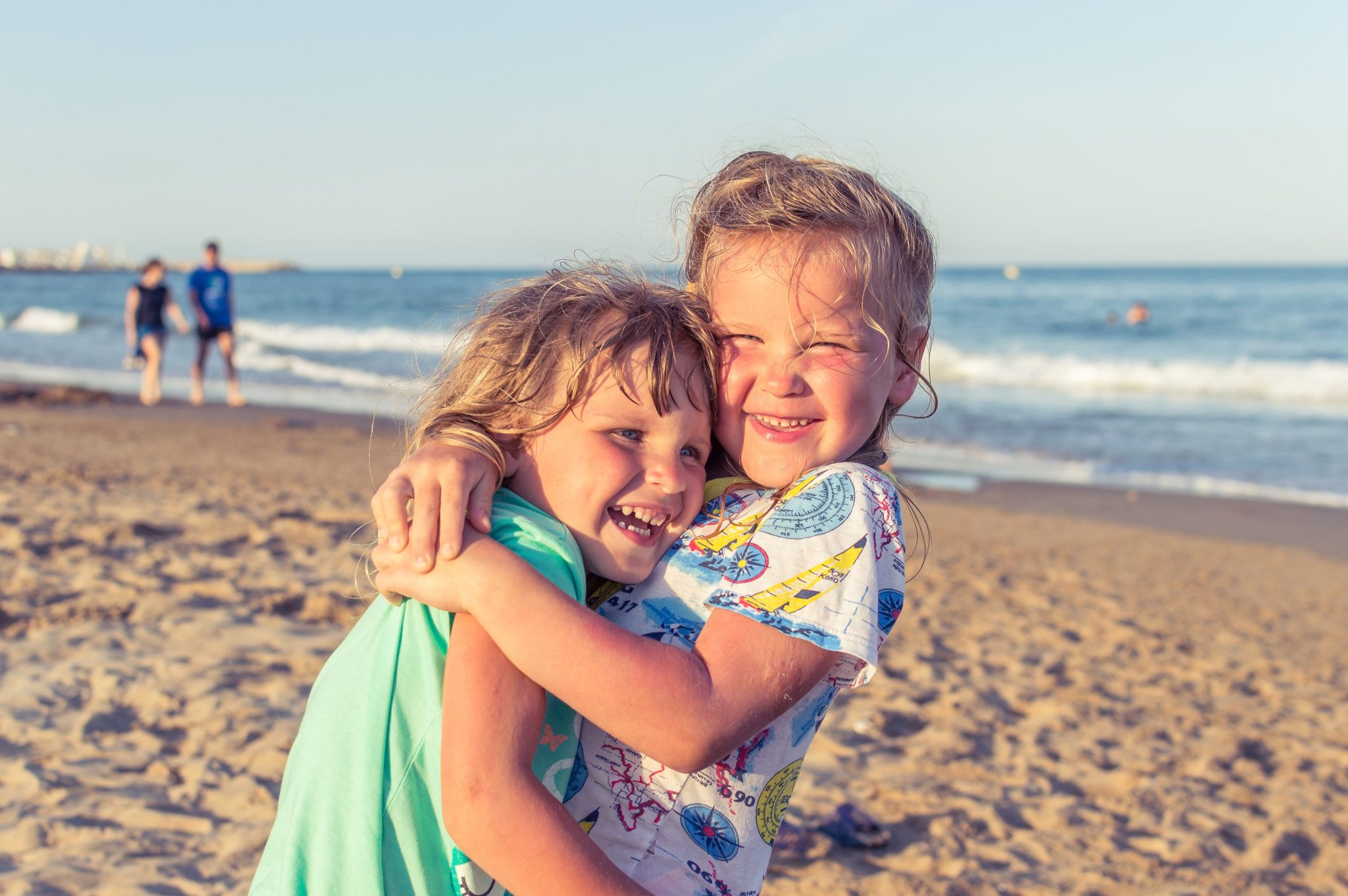 Two little girls smiling and hugging each other on the beach