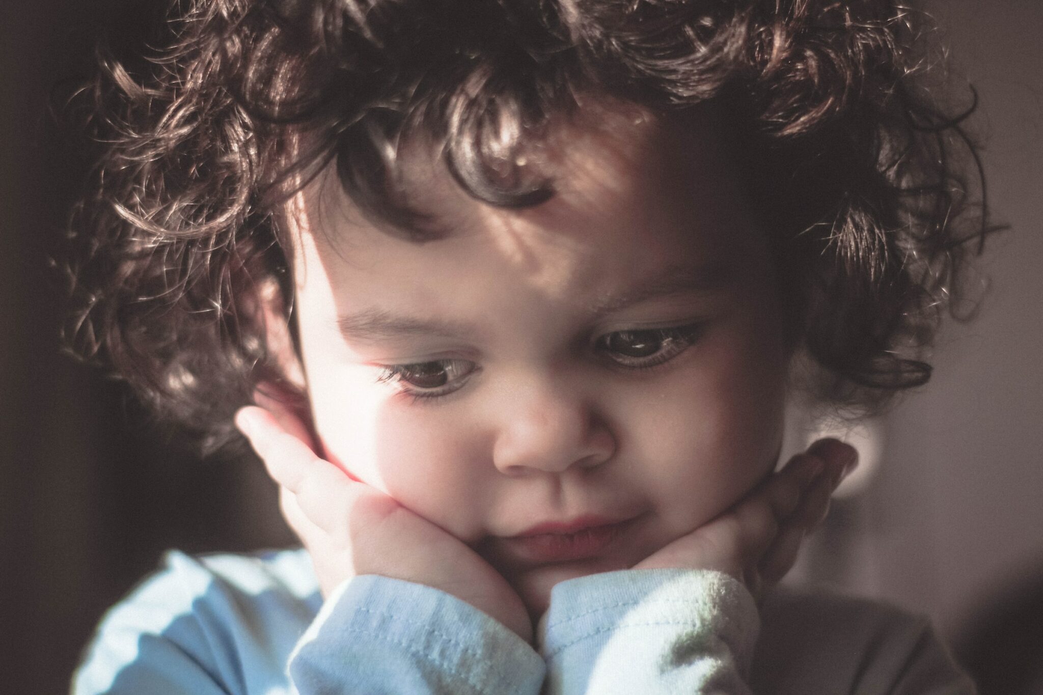 curly-haired boy with head in his hands