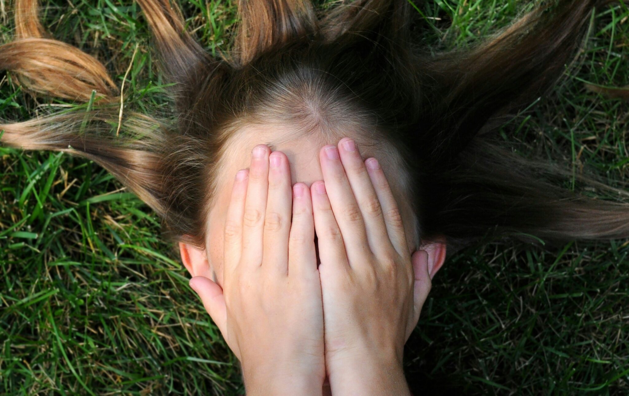 Girl lying in the grass with her hands over her face