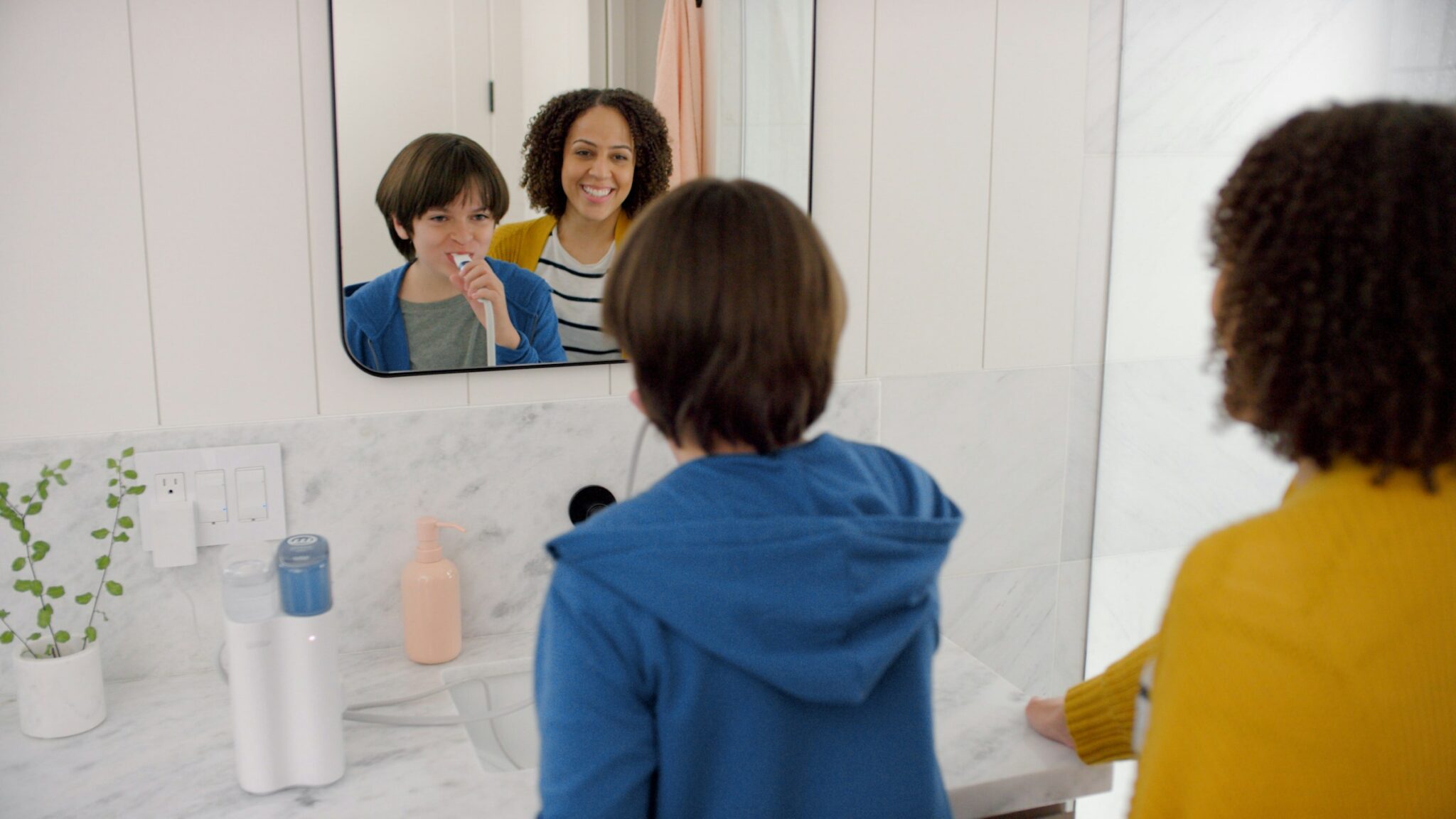Boy brushing his teeth and looking in the mirror with mom